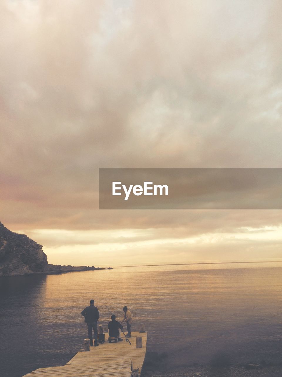 People on pier at sea against sky during sunset