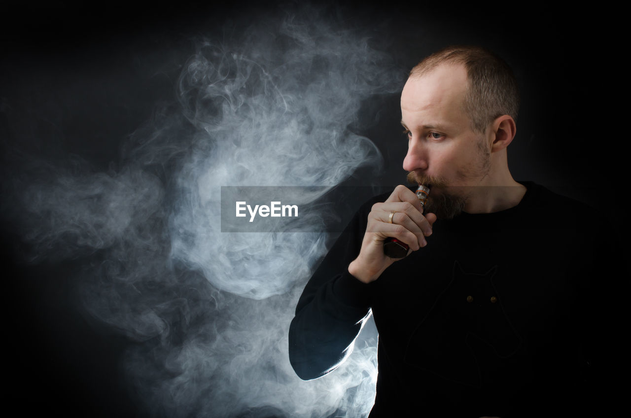 Man smoking electronic cigarette against black background