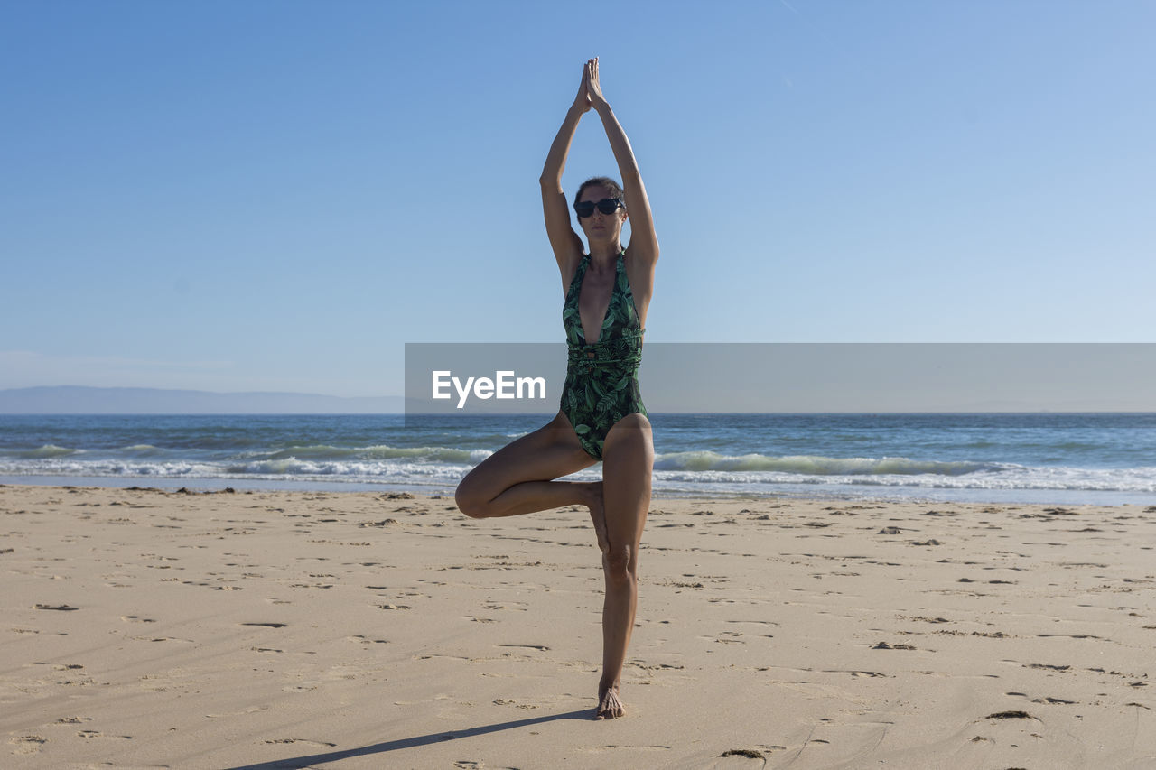 Doing yoga at the beach, the girl practices the yoga tree pose, the harmony of the body with nature.
