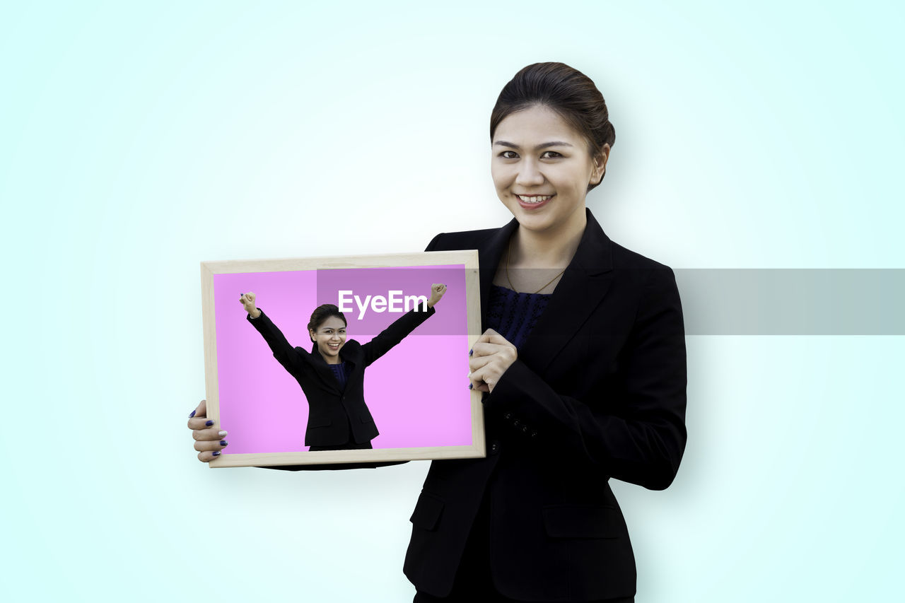 Portrait of smiling businesswoman holding billboard while standing against blue background