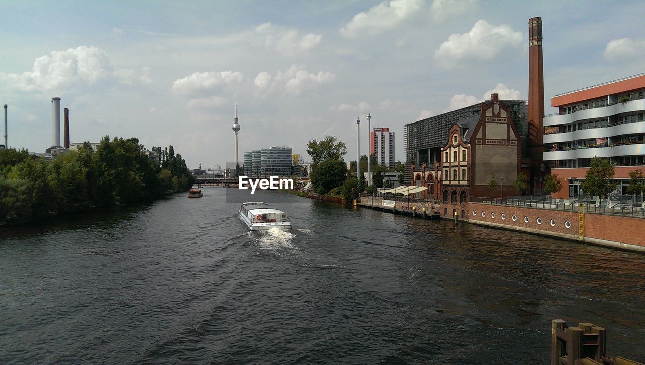 Boats sailing in river by buildings against sky