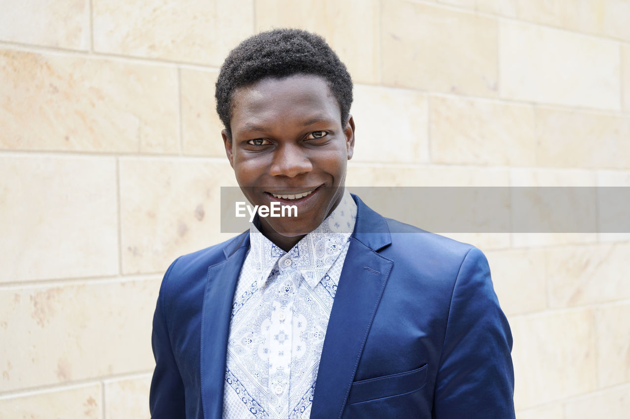 Portrait of smiling young man wearing blue blazer against wall