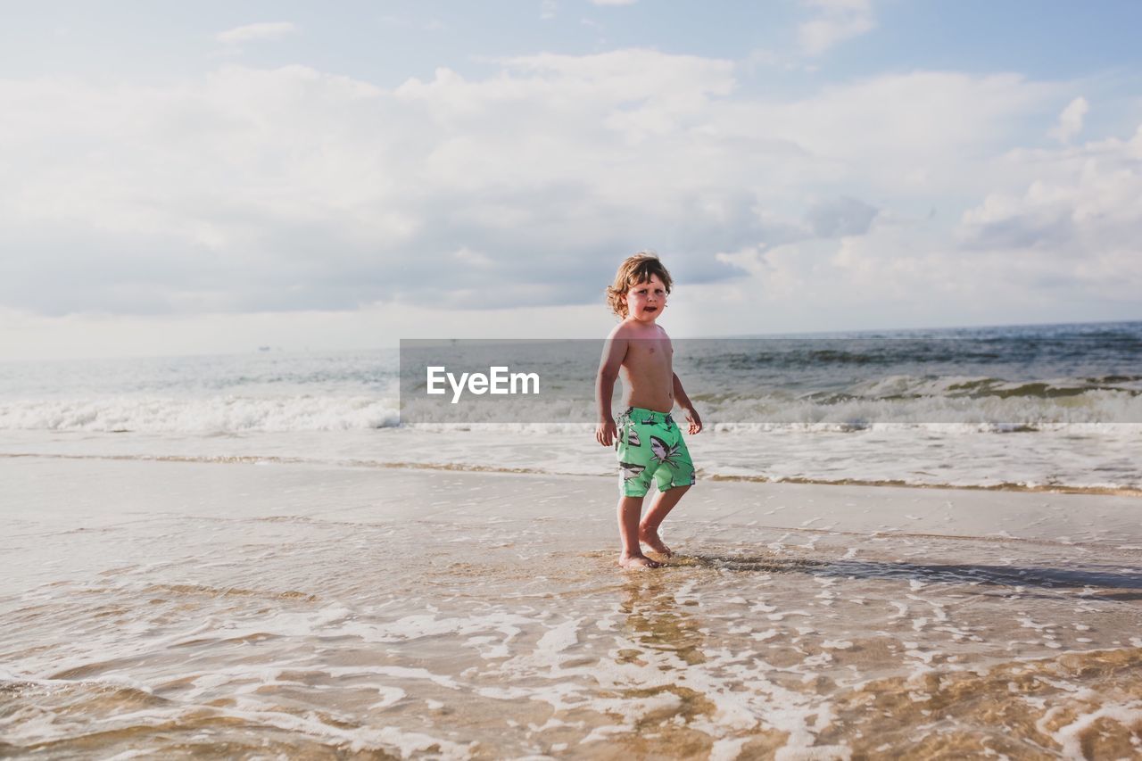 Boy walking on sand at beach against sky