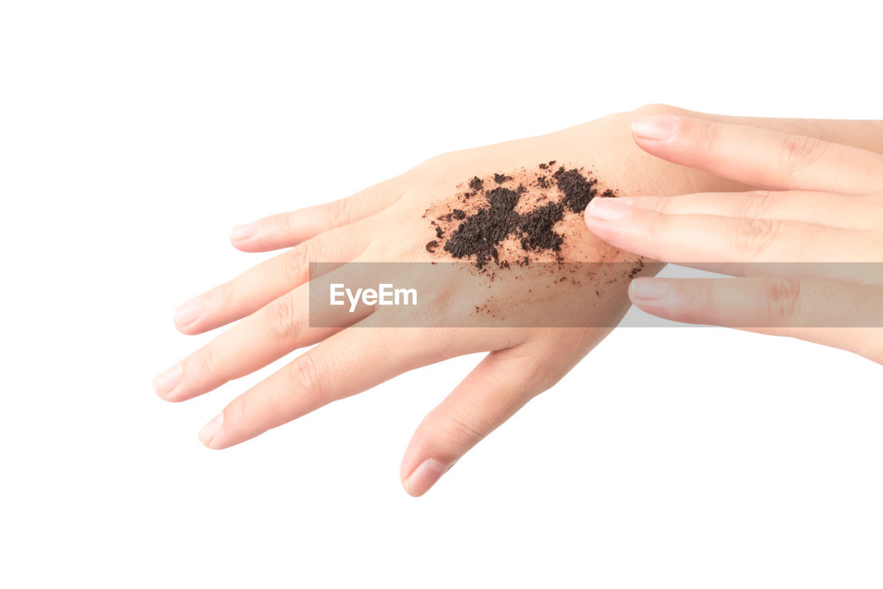 Cropped image of woman applying coffee scrub on hand against white background