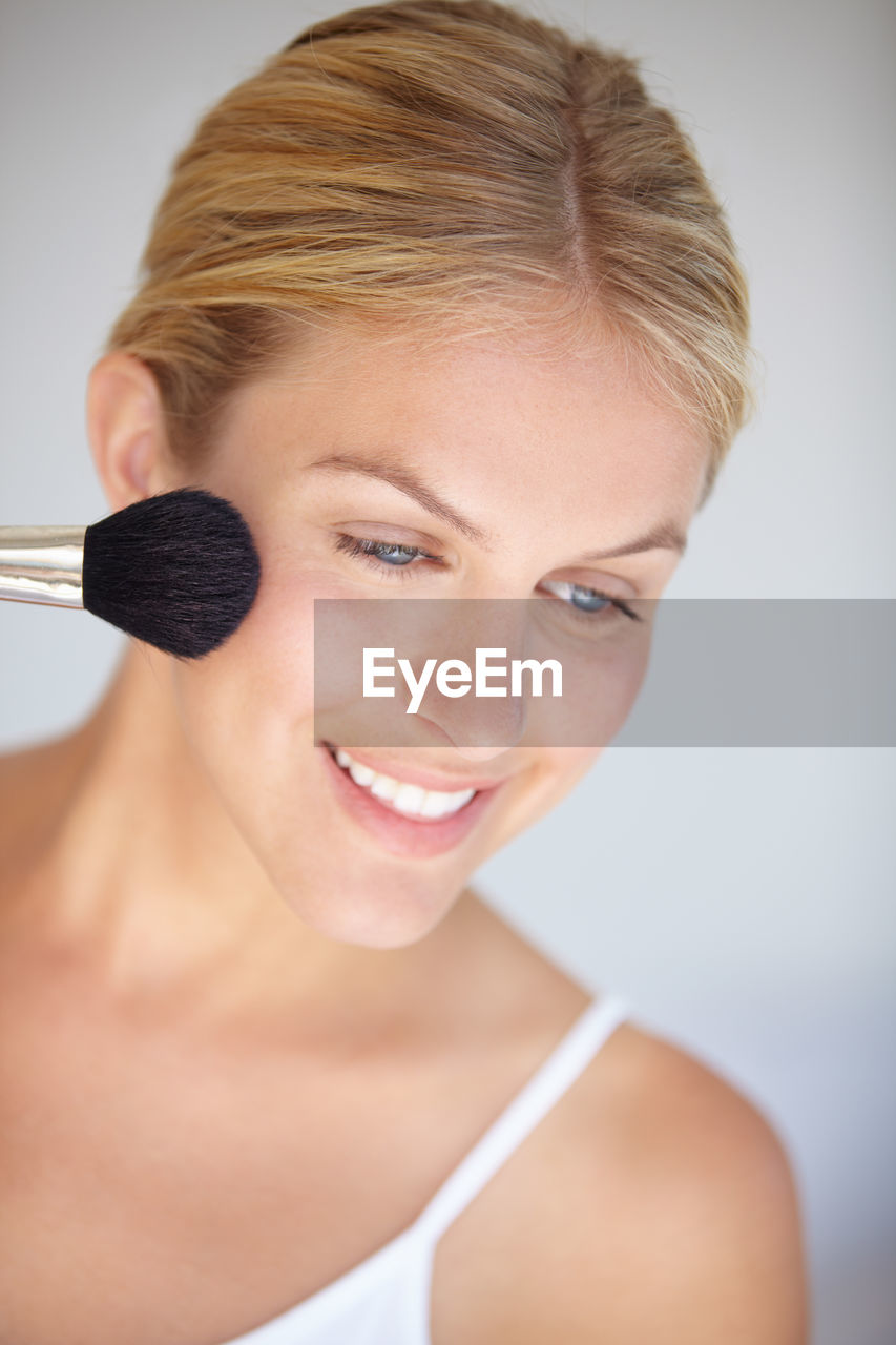 close-up portrait of young woman applying make-up against white background