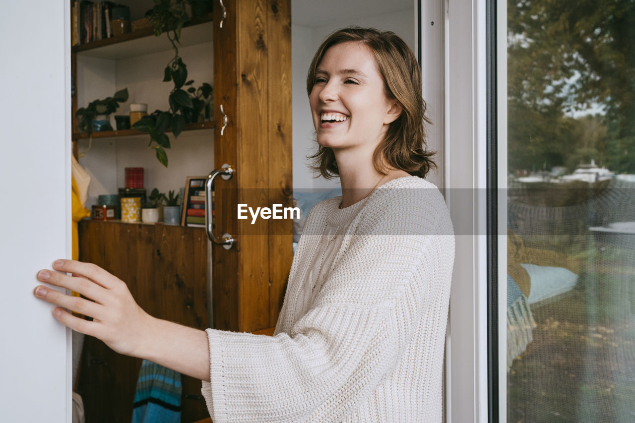 Happy young woman wearing sweater while standing at doorway