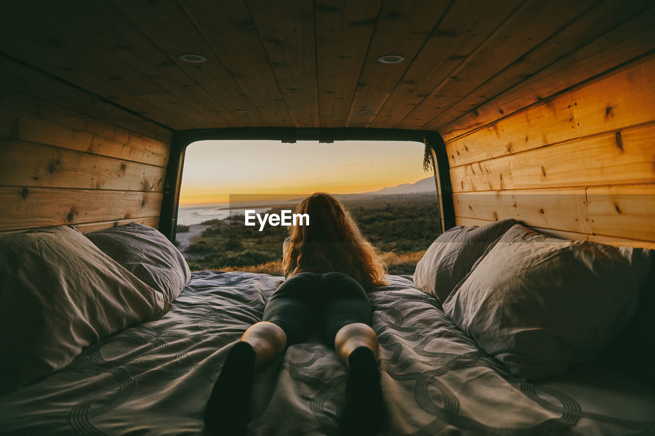 Young woman looking out to ocean from bed of camper van in mexico.