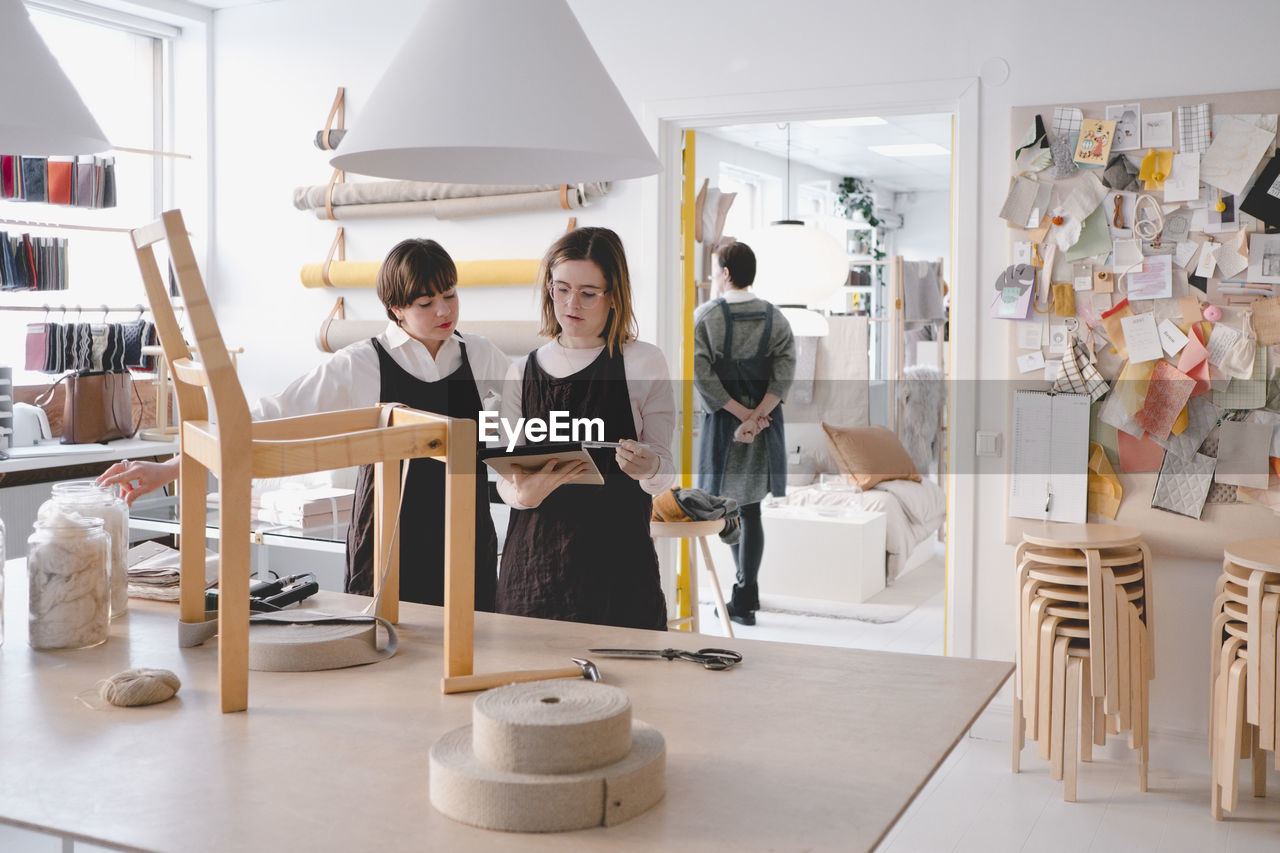 Female upholstery workers reading note pad with chair on desk in workshop