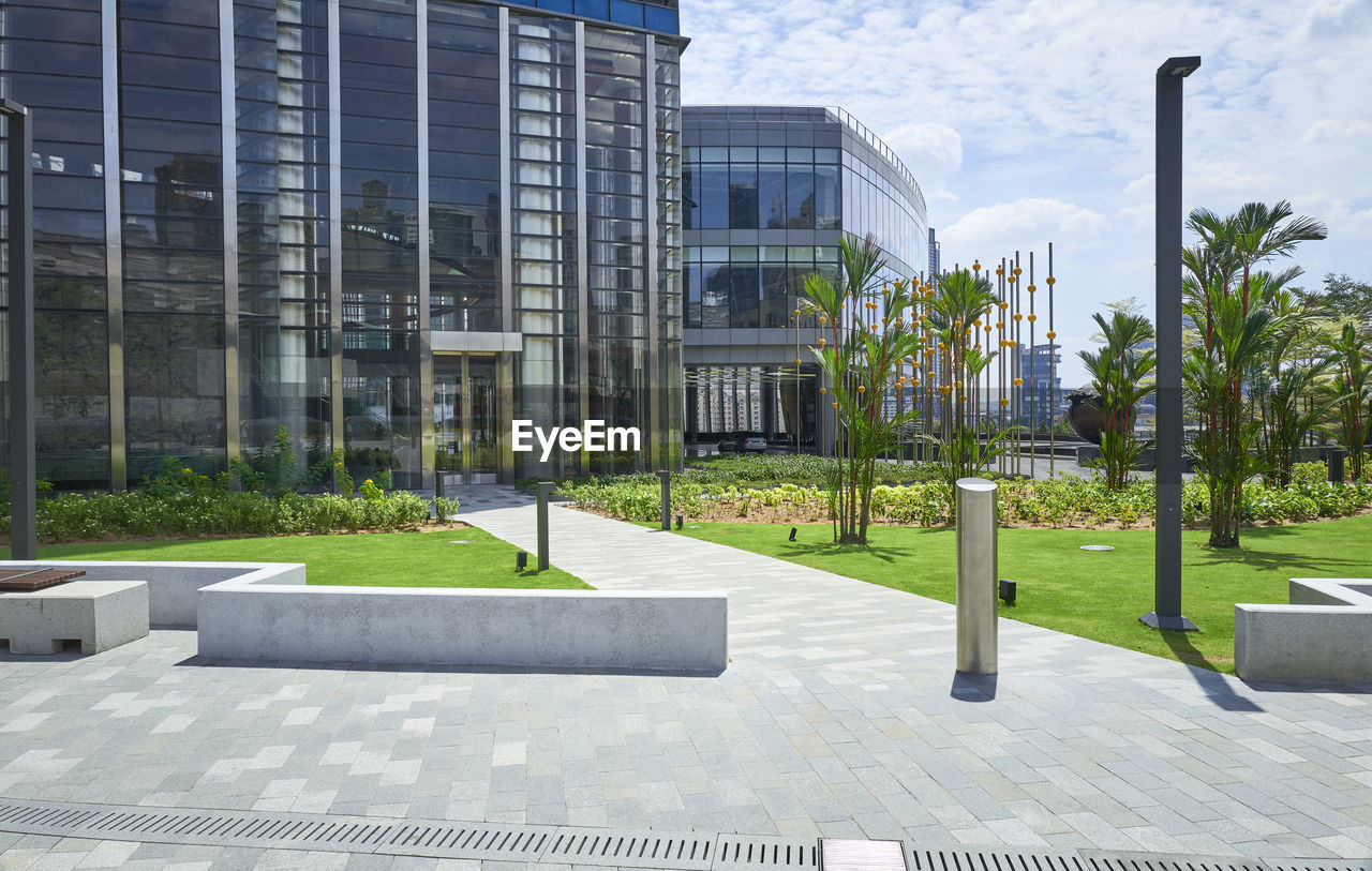 architecture, built structure, building exterior, plaza, building, condominium, city, office building exterior, sky, residential area, nature, facade, headquarters, plant, residential district, office, campus, no people, public space, outdoors, luxury, wealth, footpath, day, grass, neighbourhood, glass, tree, business, cloud, skyscraper, sunlight, entrance, city life, real estate