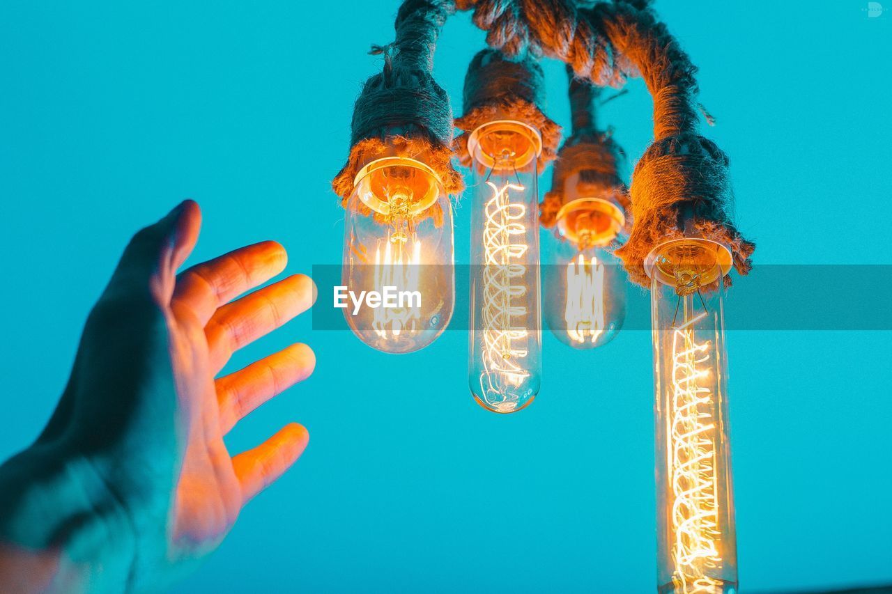 Low angle view of illuminated light bulbs against blue sky