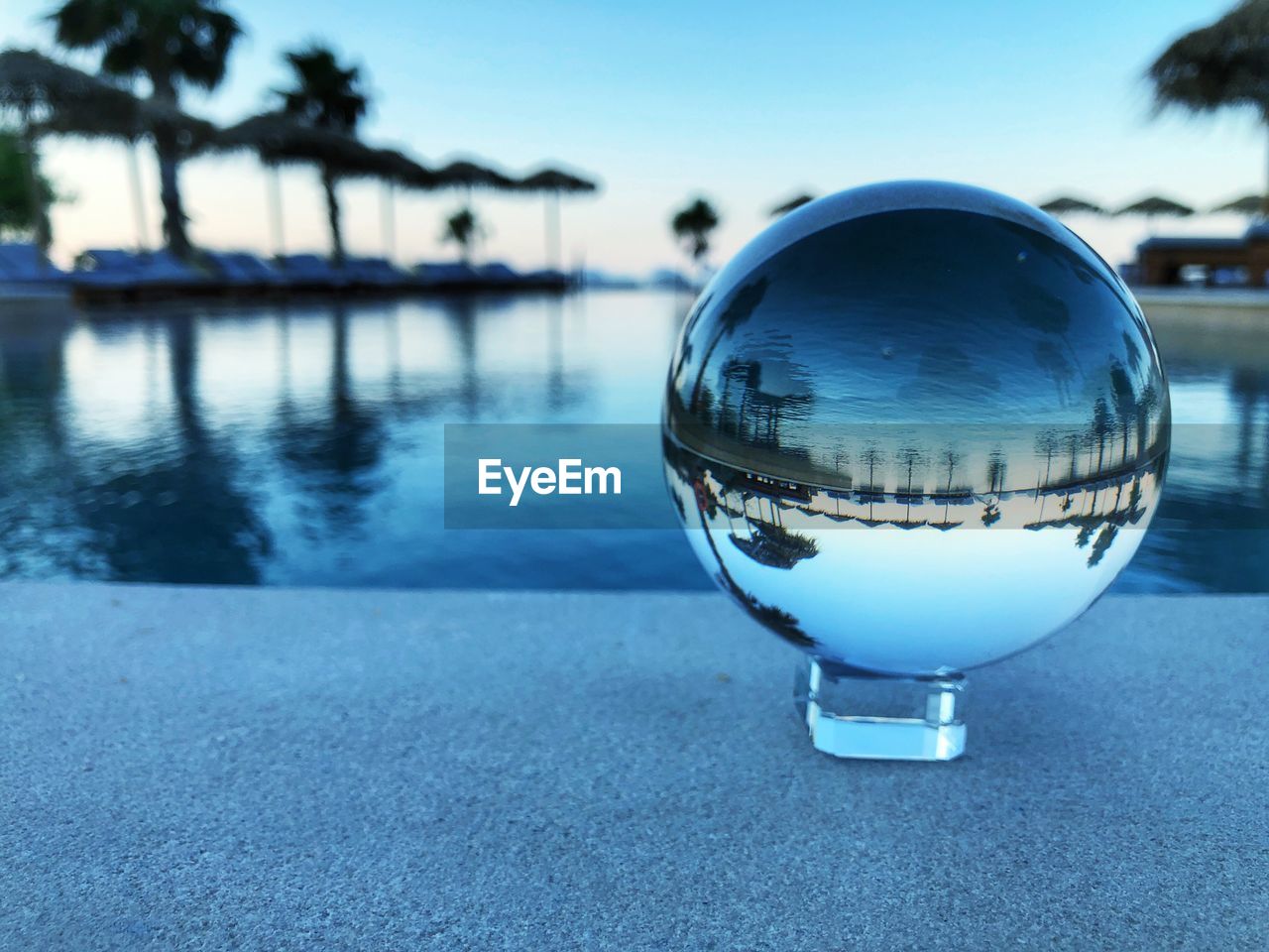 Swimming pool with palms over a horizon mirrored in a glass ball