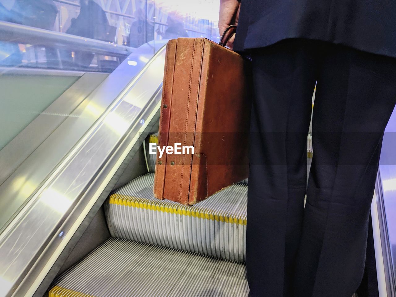 Midsection of businessman holding suitcase while standing on escalator
