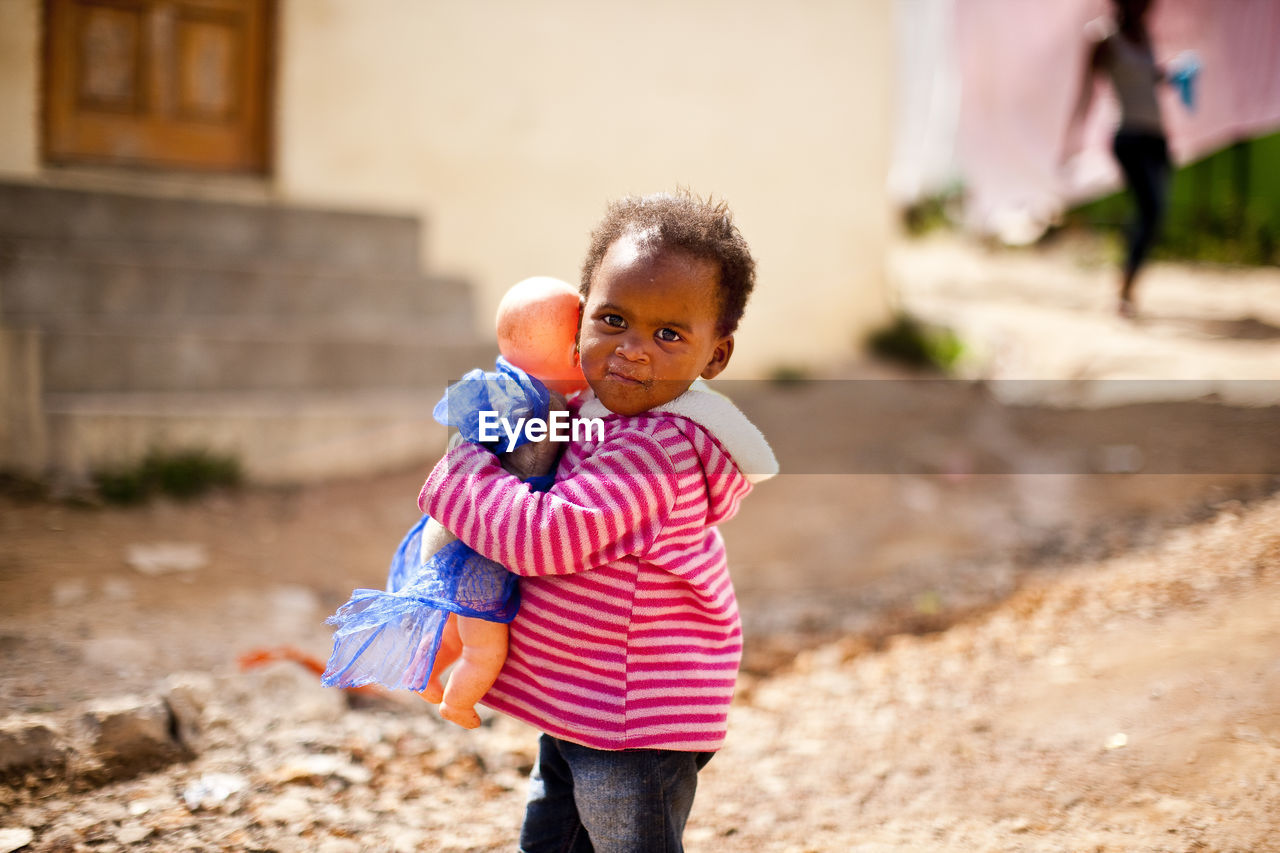 Portrait of boy with doll on footpath in town