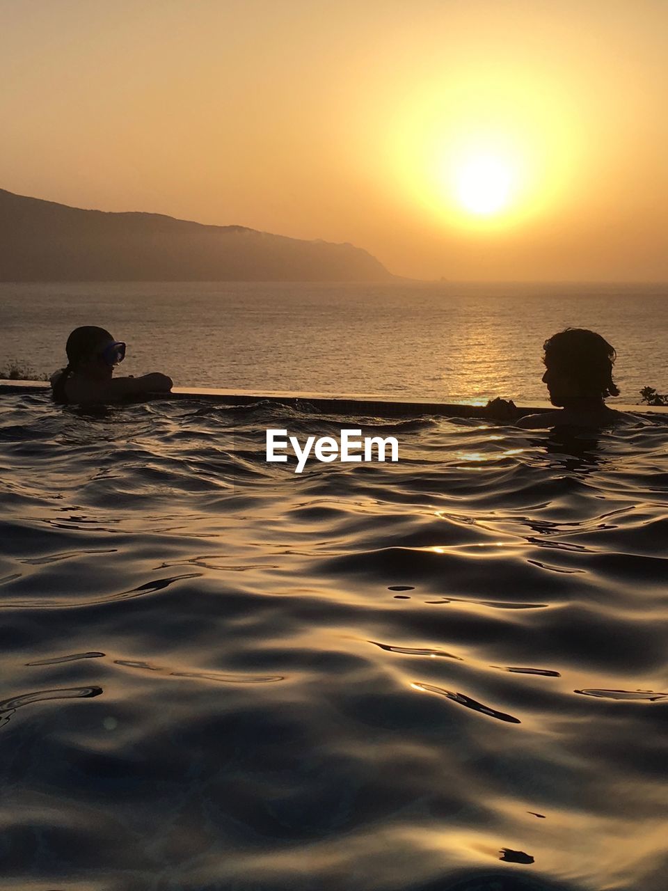 People in pool against sea during sunset