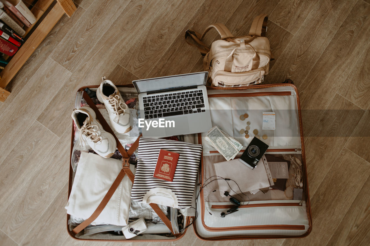 Open baggage with snickers, sweater, laptop, headphones and passport, vintage camera and backpack.