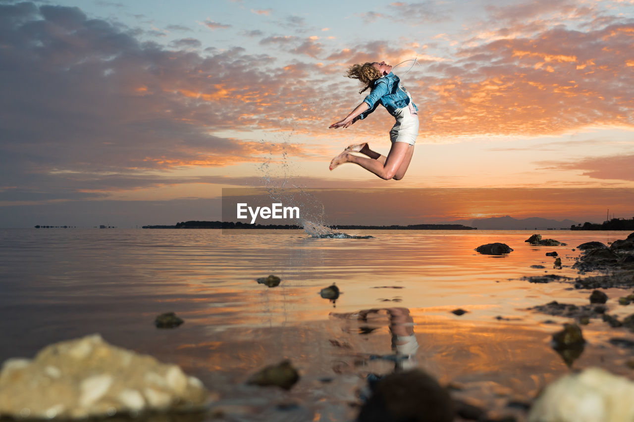 Woman jumping on beach against sky during sunset