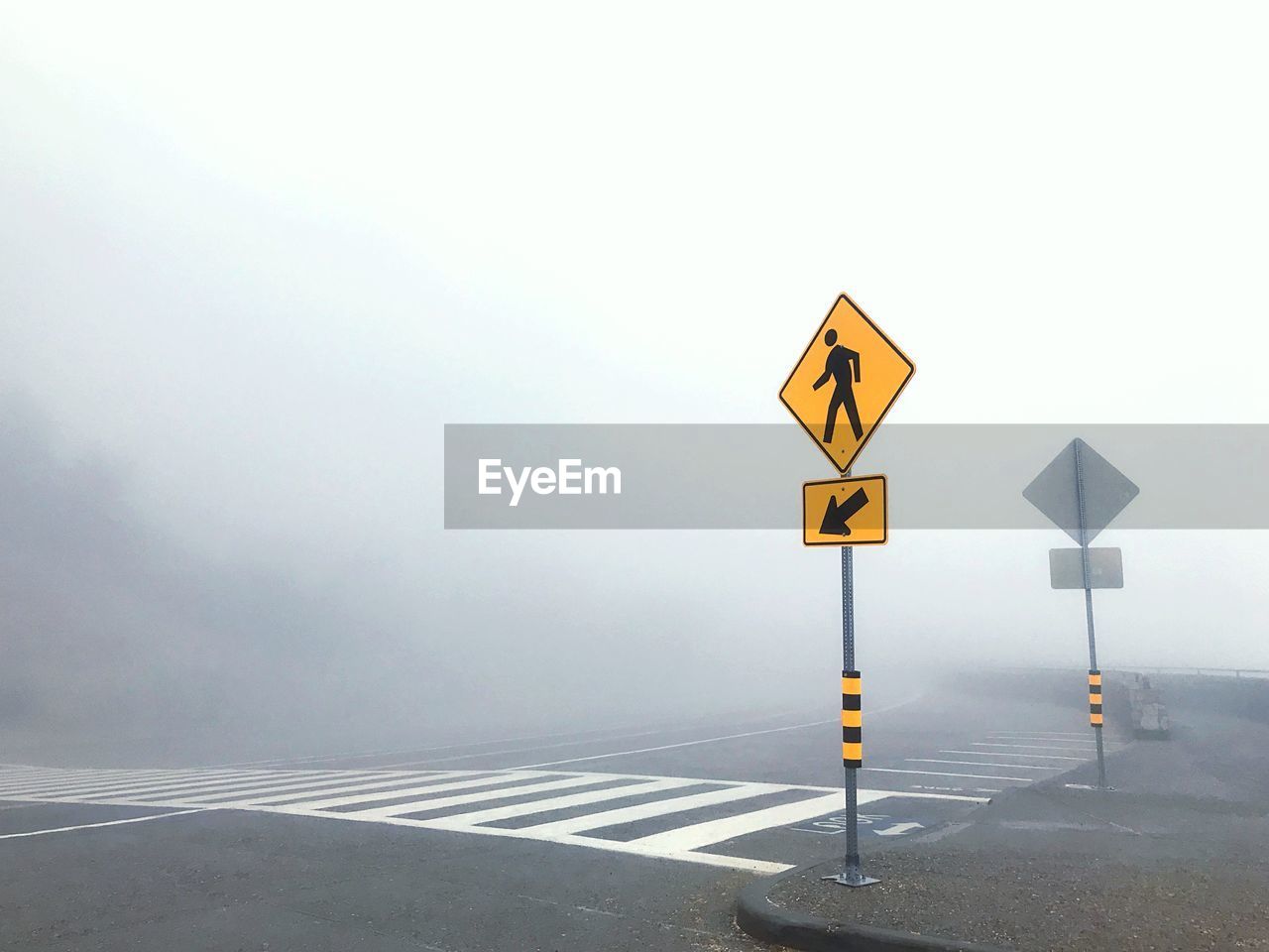 Road sign against clear sky during foggy weather