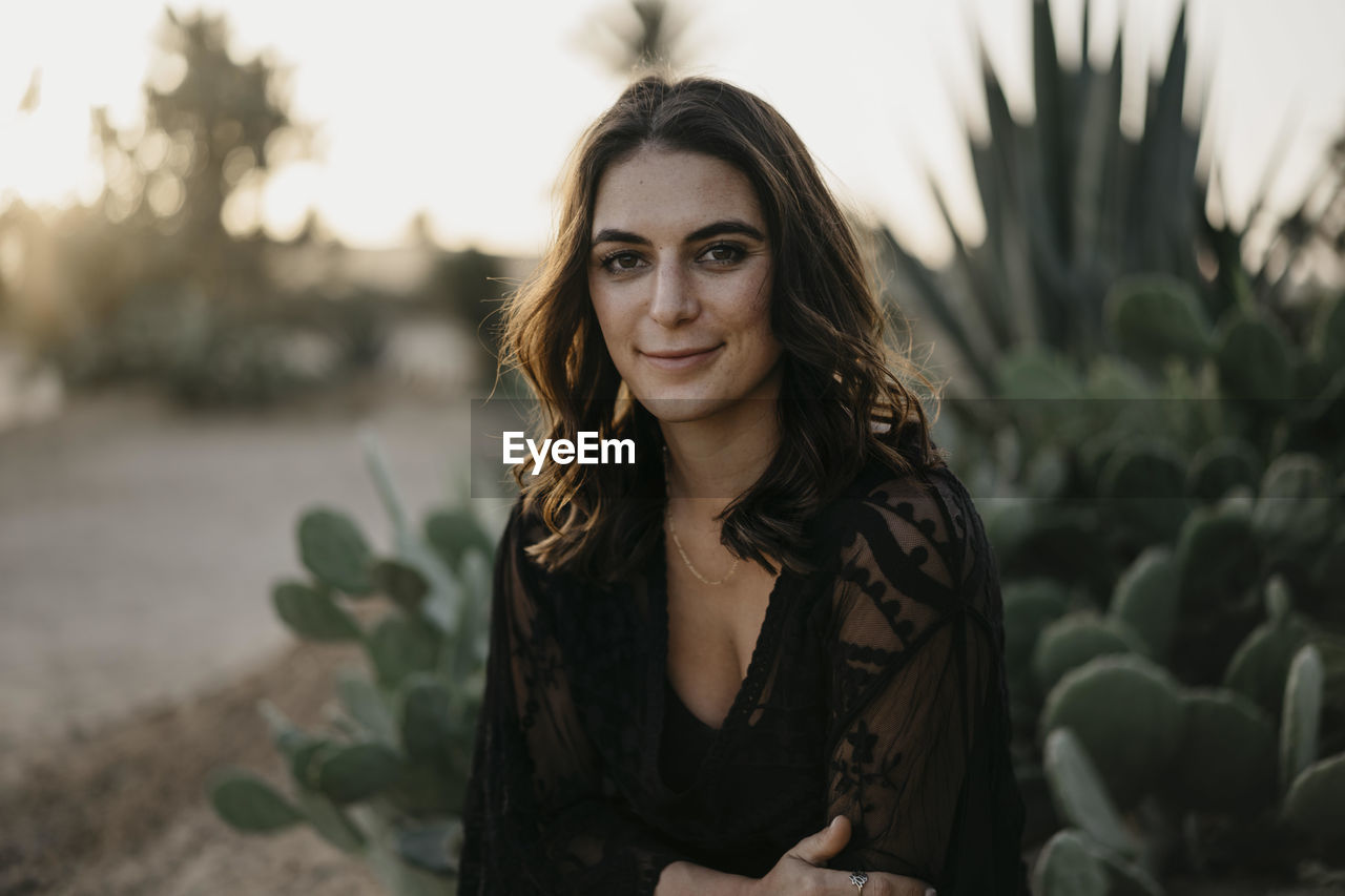 Smiling beautiful woman against cactus plants at sunset