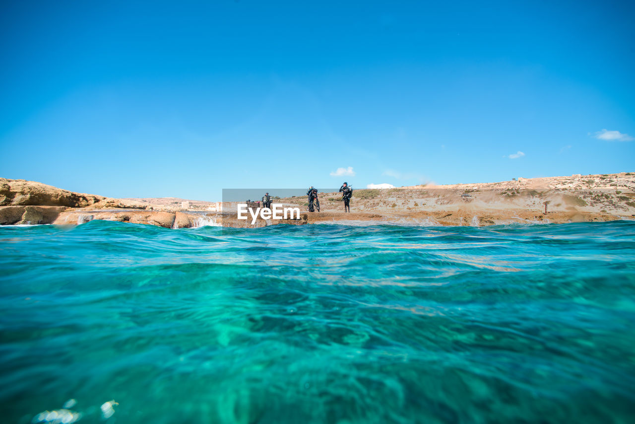 Mid distance view of scuba divers standing by sea against sky