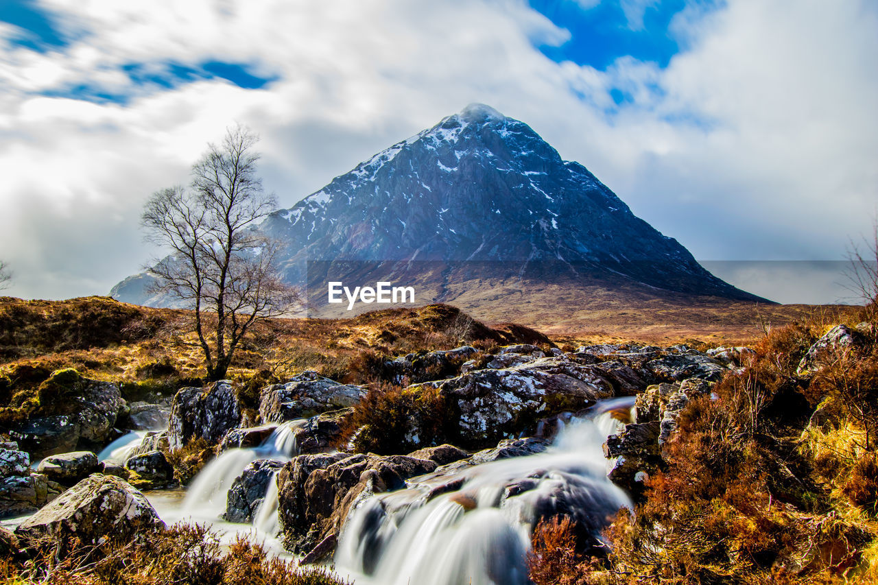 Scenic view of waterfalls and mountains against cloudy sky