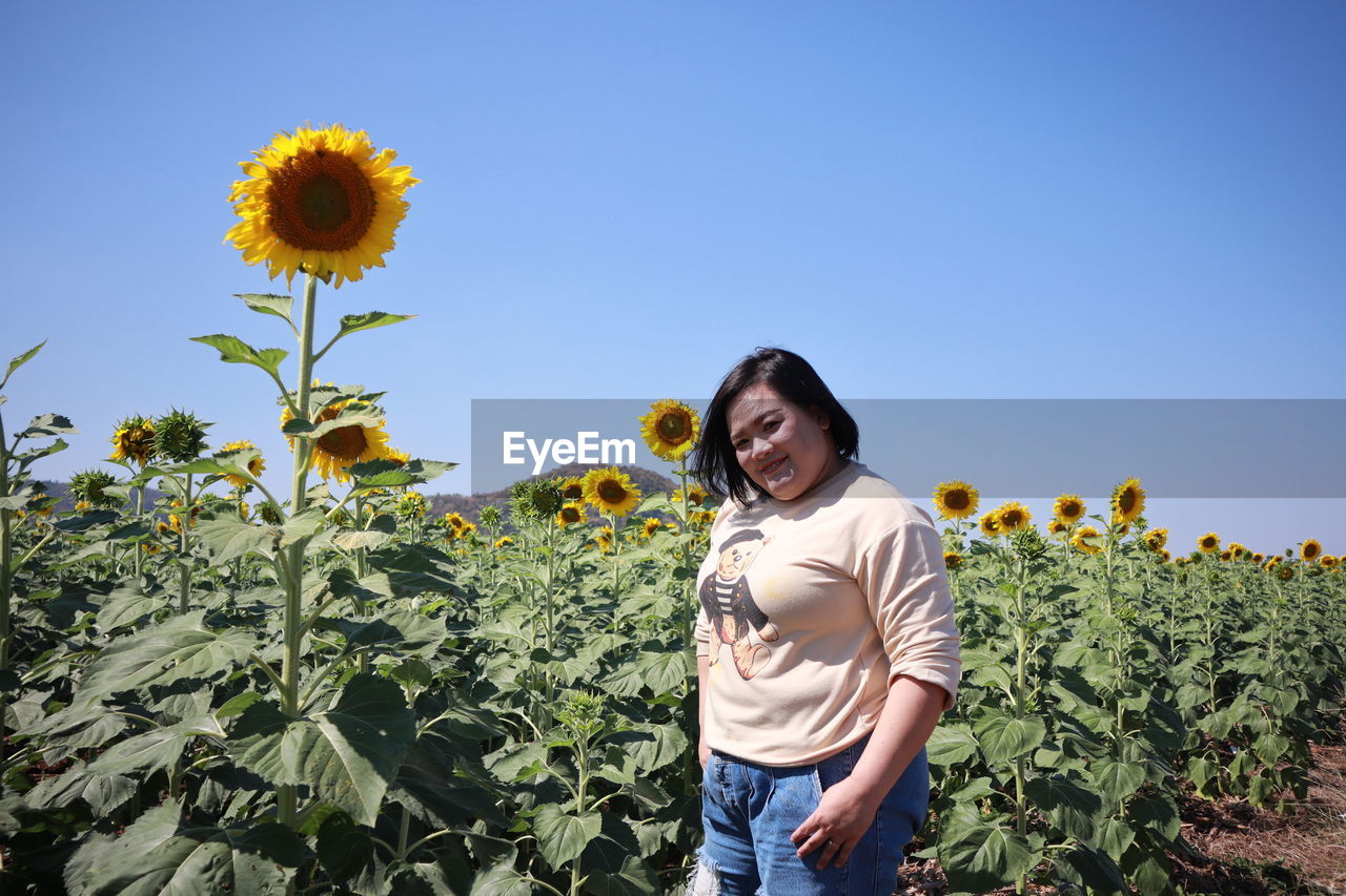 Portrait of beautiful woman standing by sunflower field against clear sky