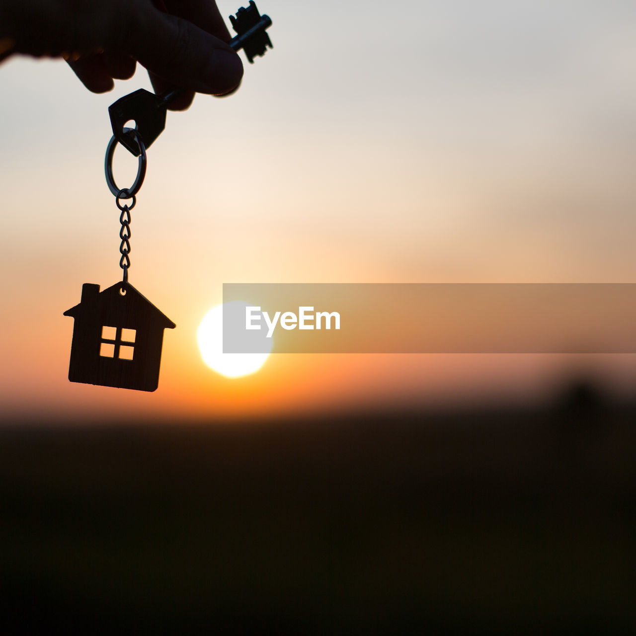 Silhouette of a house figure with a key, a pen with a keychain on the background of the sunset. 