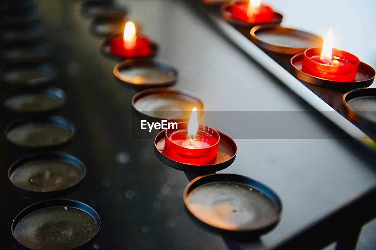 HIGH ANGLE VIEW OF ILLUMINATED TEA LIGHT CANDLES ON DISPLAY