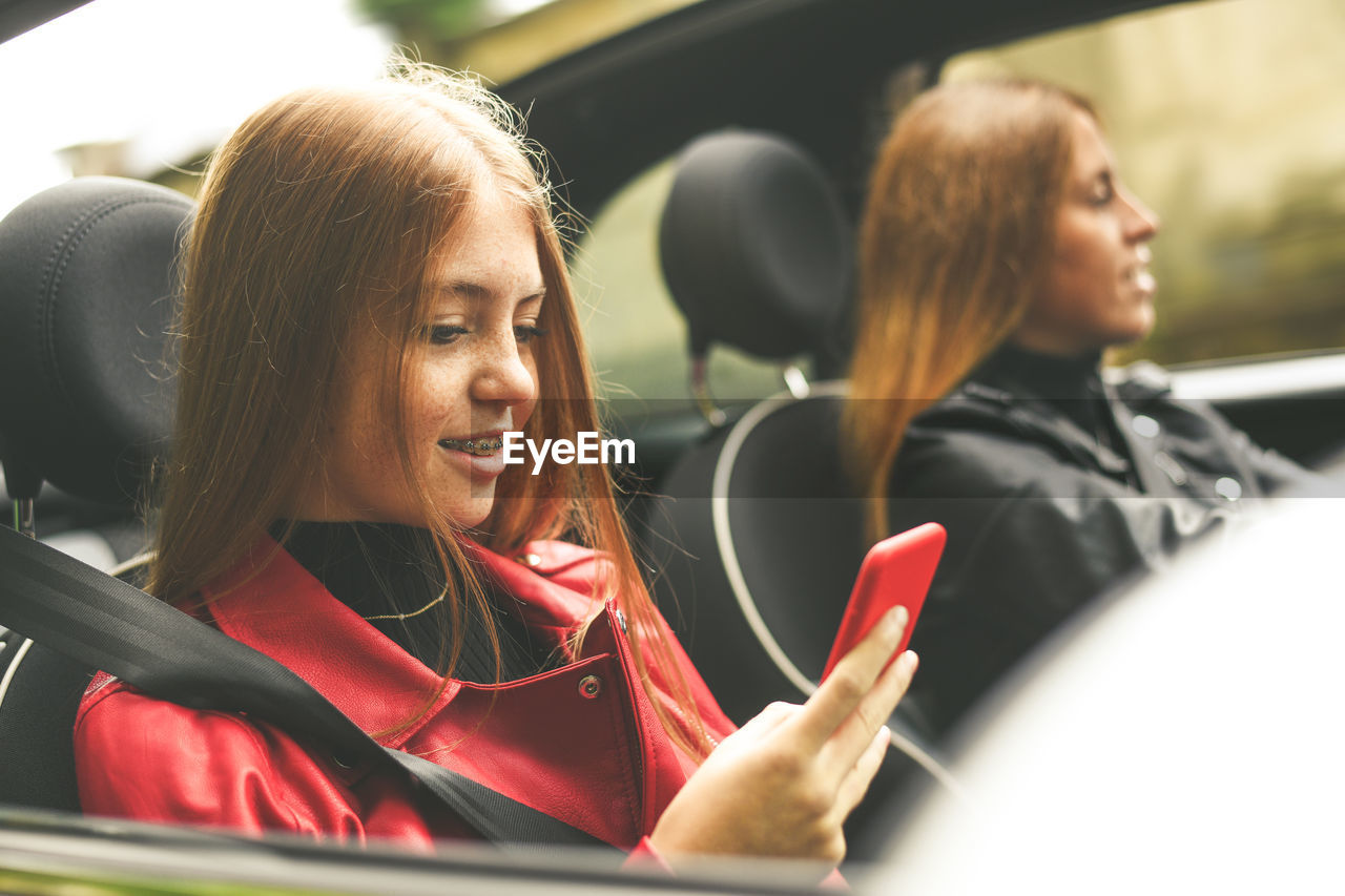 Girls sitting in the car. smiling teen in front of the steering wheel young women using smartphone