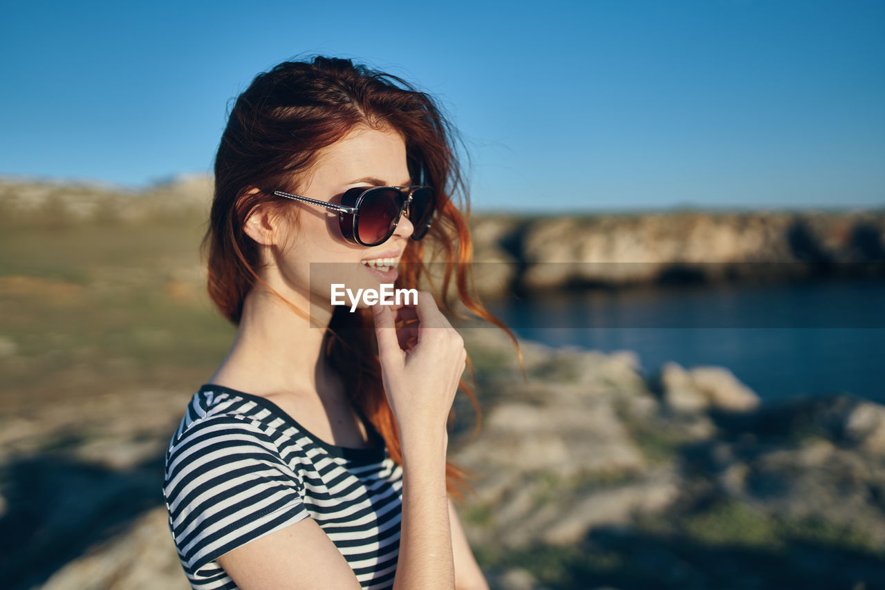 PORTRAIT OF WOMAN WEARING SUNGLASSES AT BEACH