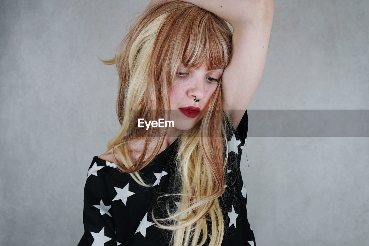 Thoughtful young woman with blond hair against gray background