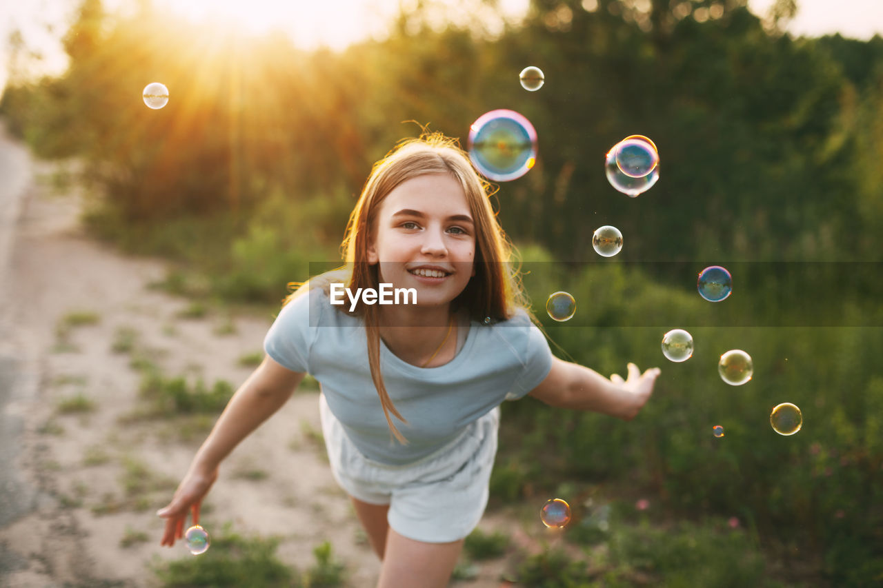 Portrait of smiling girl playing with bubbles in park at sunset