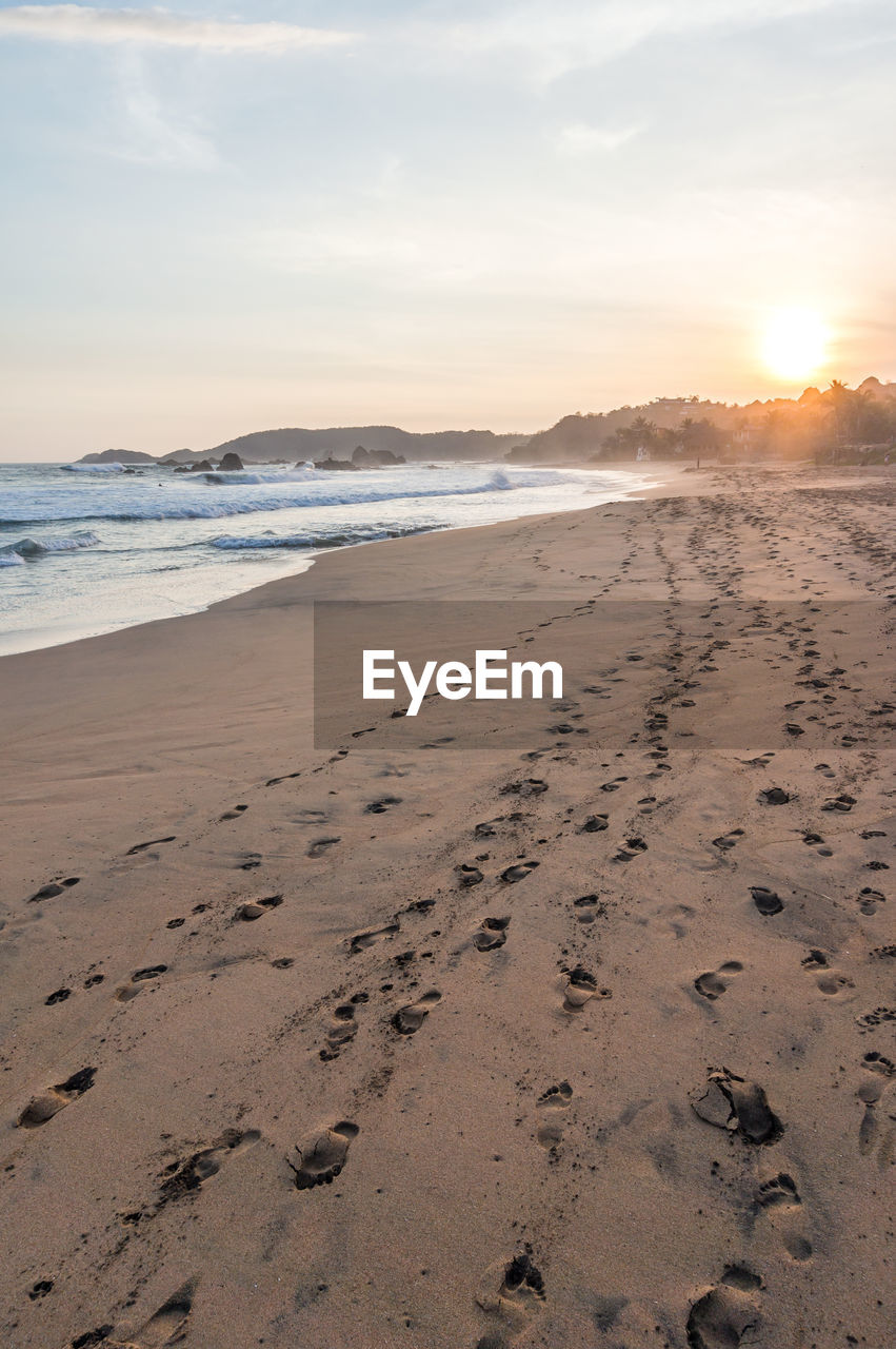 Footprints on sand at beach against sky during sunset