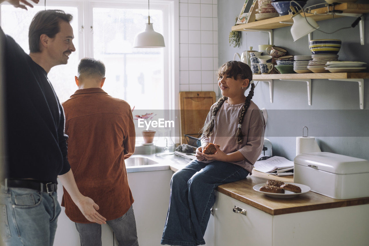 Father playing with daughter holding bread while sitting on kitchen counter at home