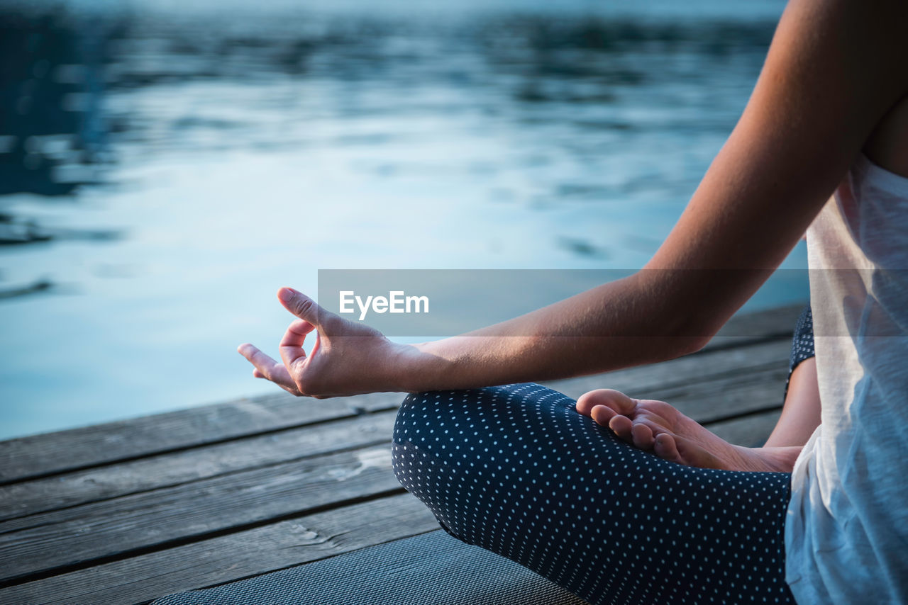 Low section of woman practicing yoga on pier over lake