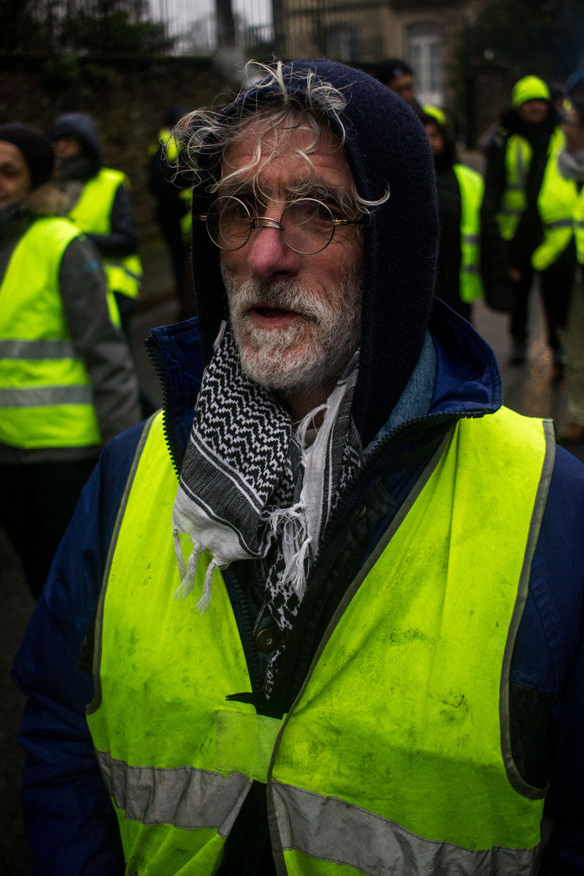 reflective clothing, clothing, adult, men, person, portrait, yellow, facial hair, beard, green, focus on foreground, one person, protection, occupation, human face, mature adult, waist up, standing, looking at camera, jacket, outdoors, day, security, protective workwear, glasses, serious, front view