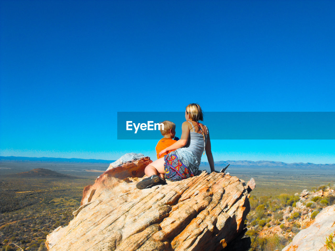 REAR VIEW OF PEOPLE ON ROCK AGAINST BLUE SKY