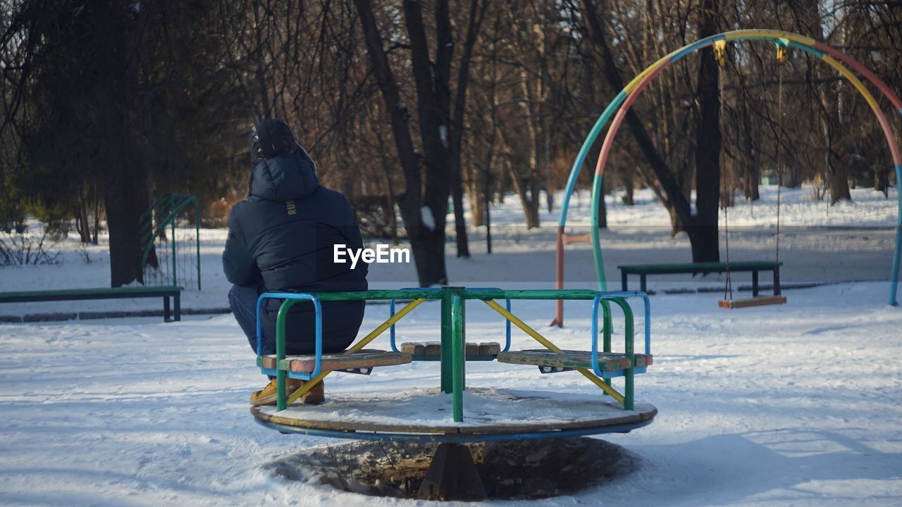 Rear view of man sitting on play equipment during winter