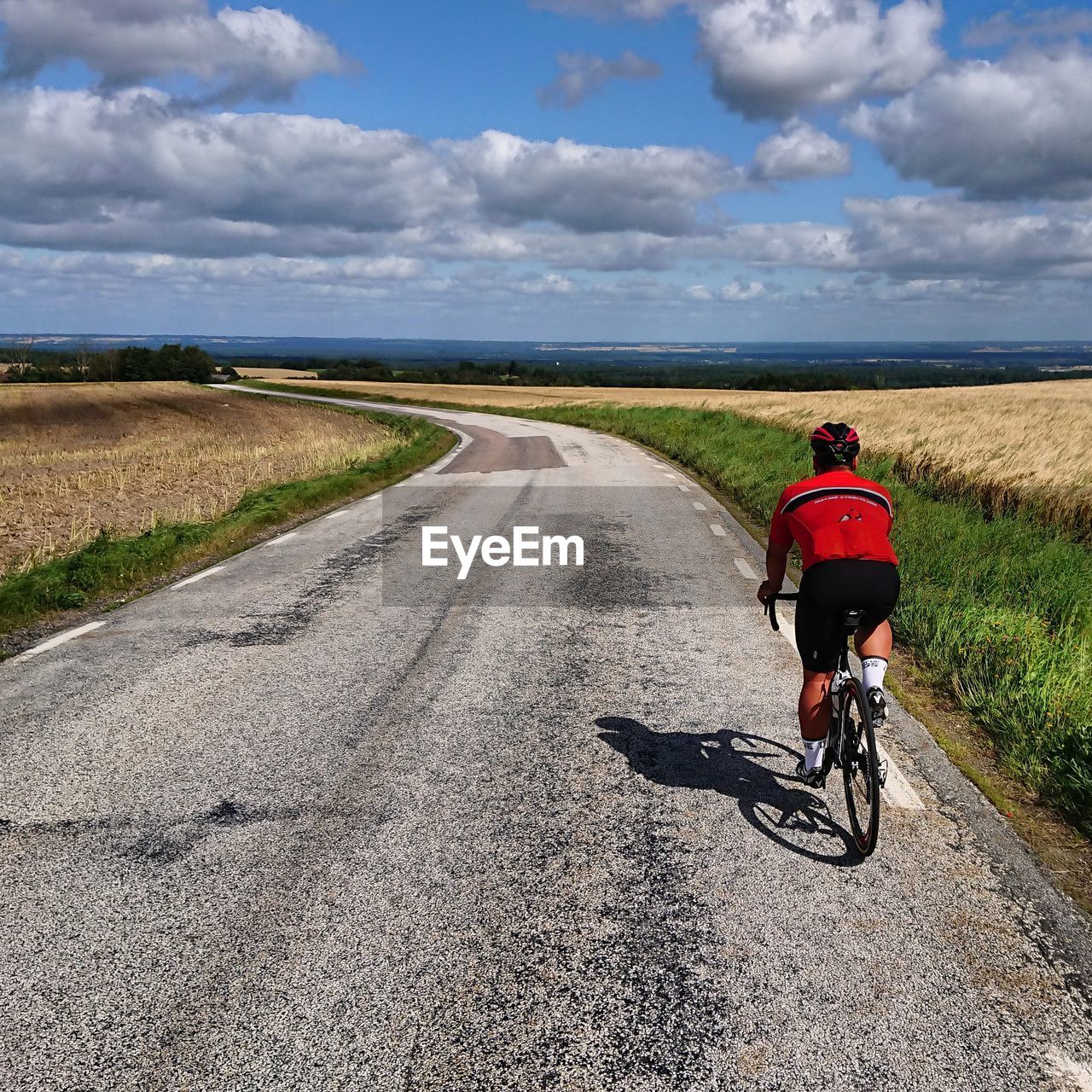 Rear view of man riding bicycle on road against sky