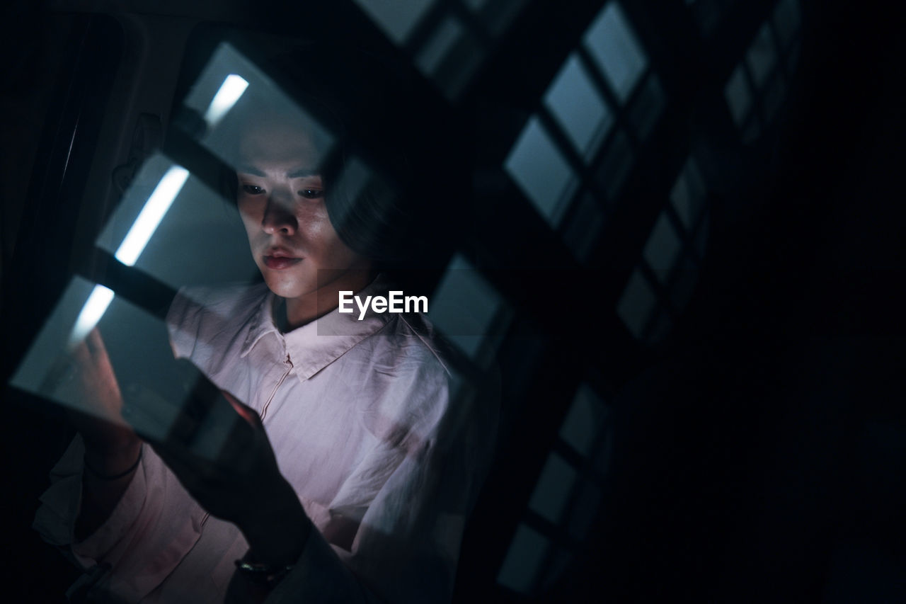 Young man with smart phone seen through glass at night