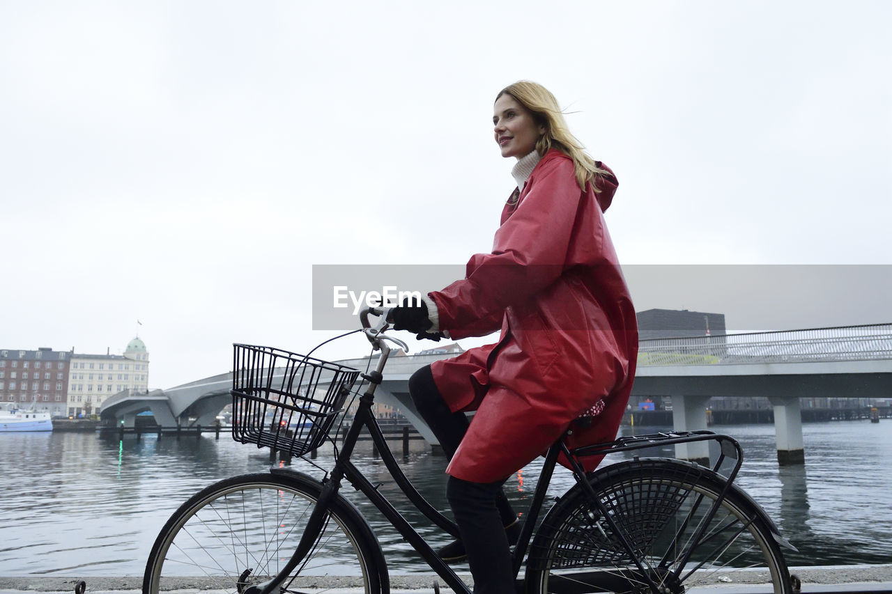 Denmark, copenhagen, woman riding bicycle at the waterfront in rainy weather