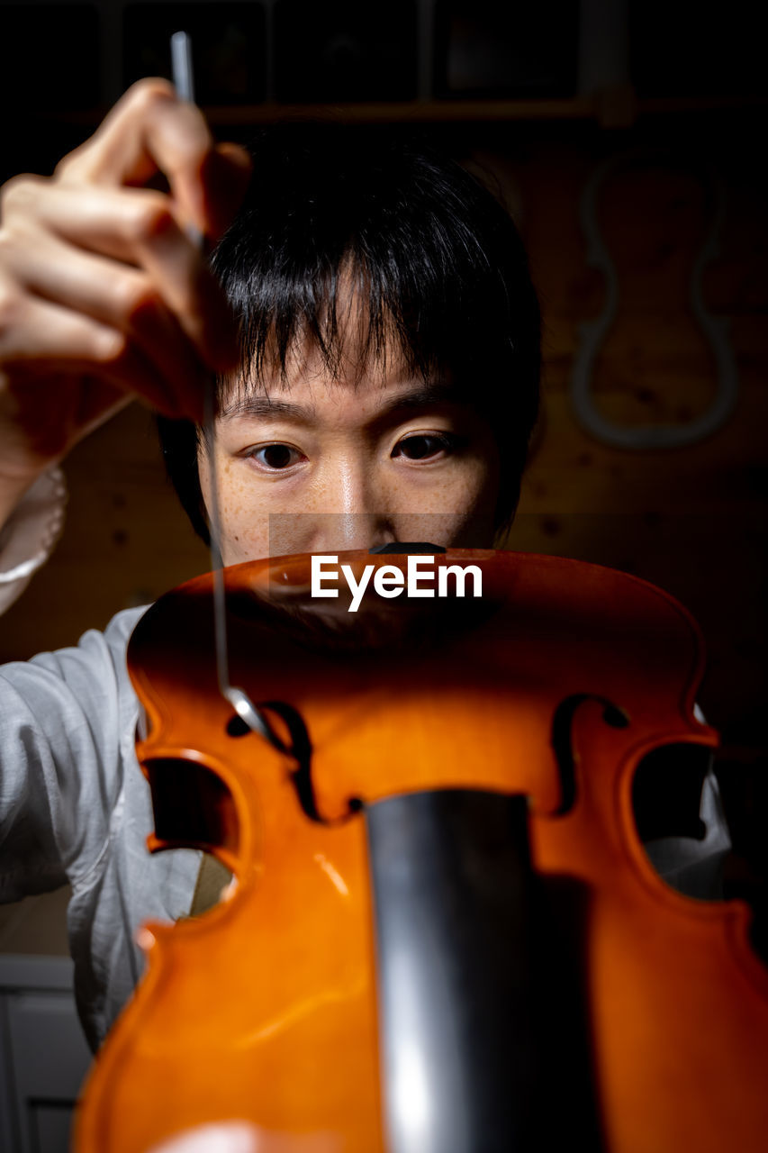 Young chinese woman violin maker checking the quality of her violin in the workshop