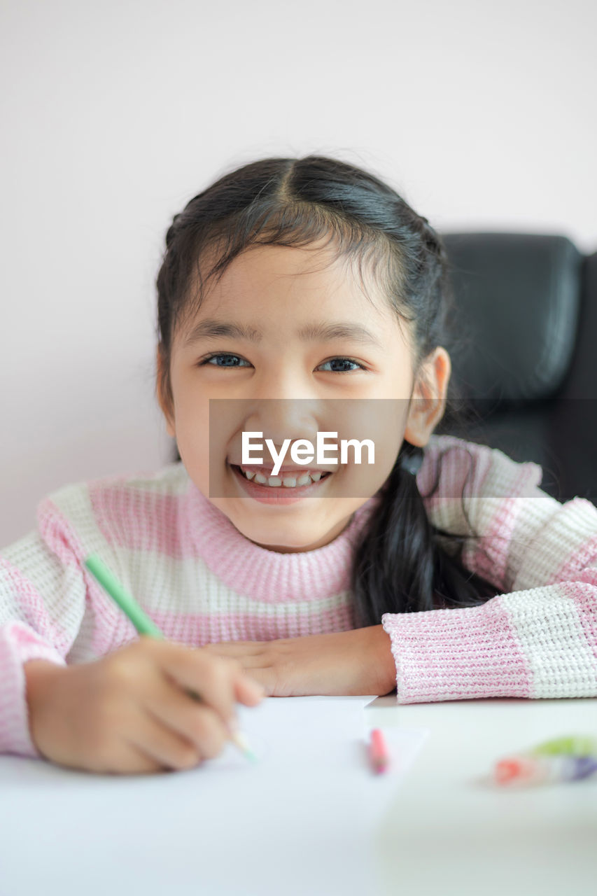 Portrait of smiling cute girl holding pencil on table