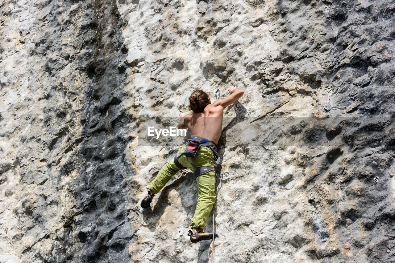 Rear view of shirtless man climbing on rock