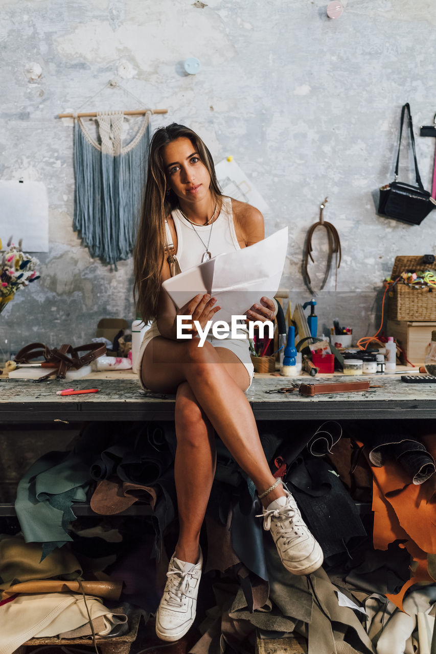 Fashion designer holding paper and tablet pc sitting on workbench