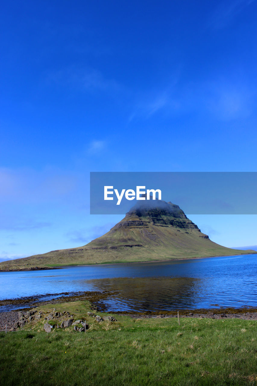 Scenic view of sea and mountains against blue sky. kirkjufell