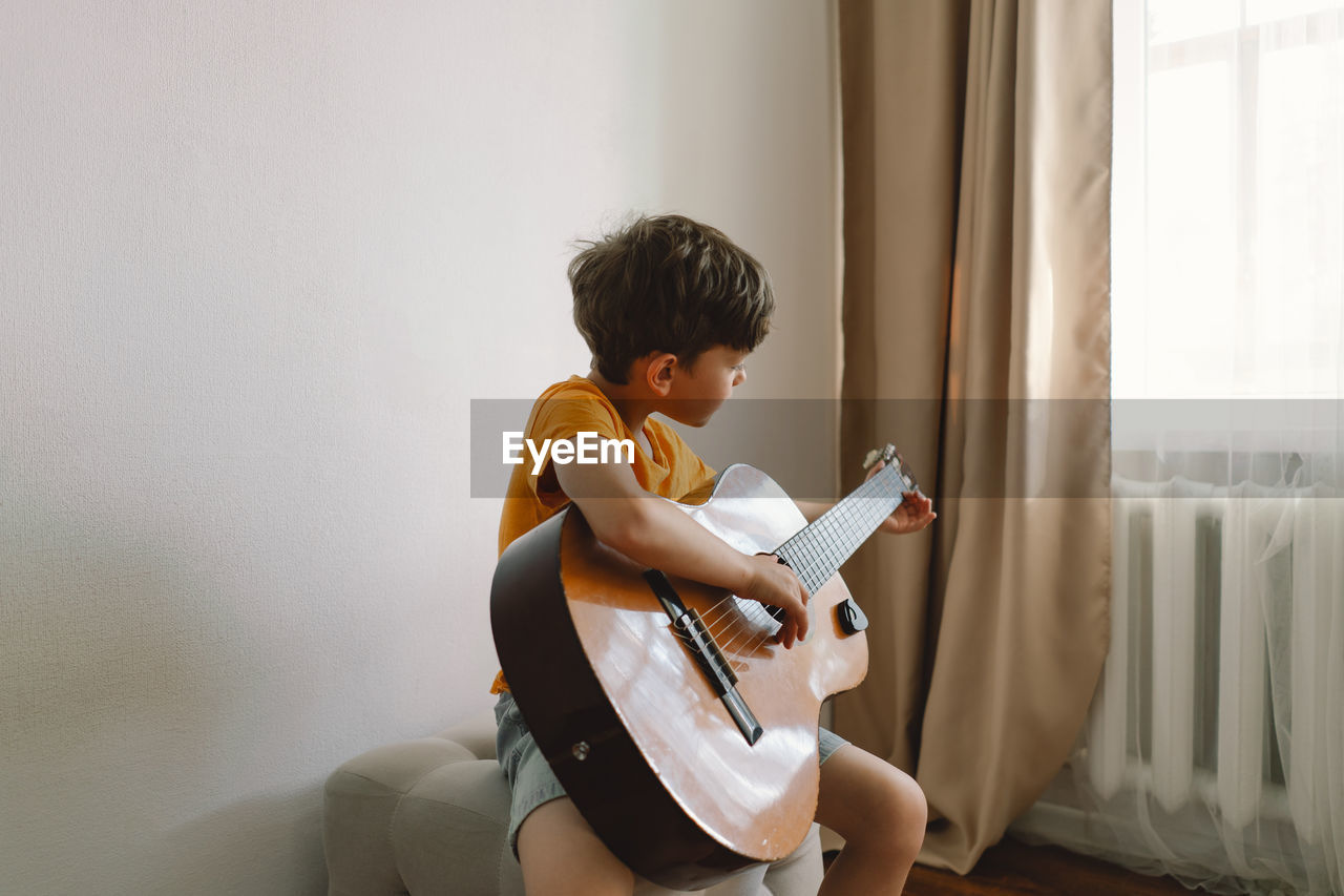 Cute boy learns to play the classical guitar in home. cozy home.