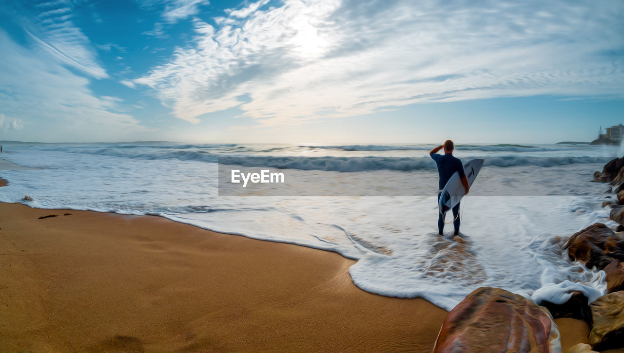 Man carrying surfboards while standing at beach against sky