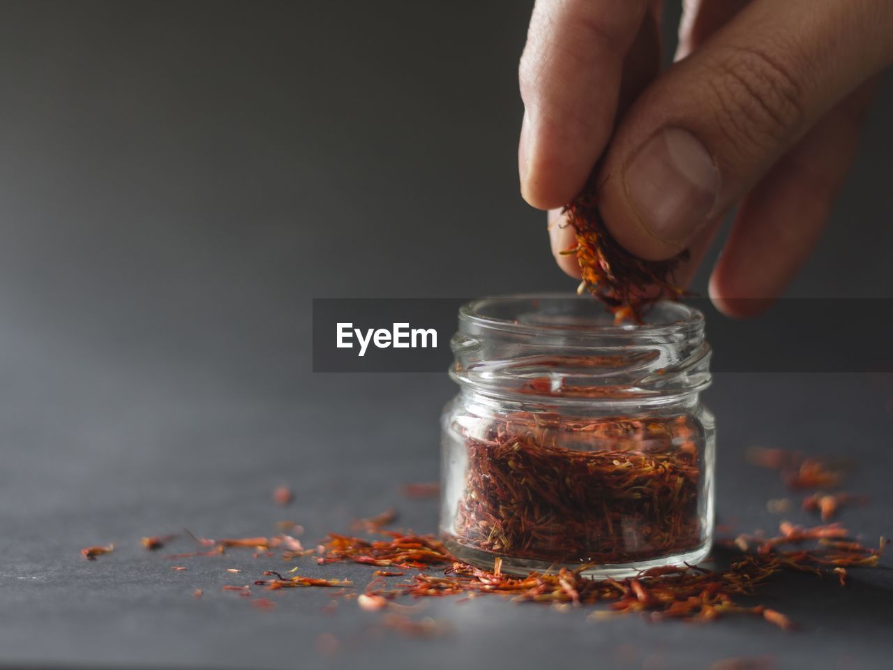 Close-up of human hand removing saffron from bottle on table