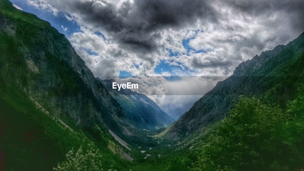 Scenic view of valley and mountains against cloudy sky