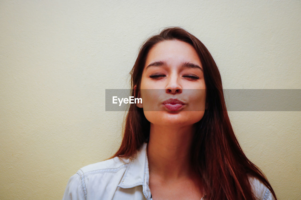 Close-up of woman with eyes closed puckering against wall